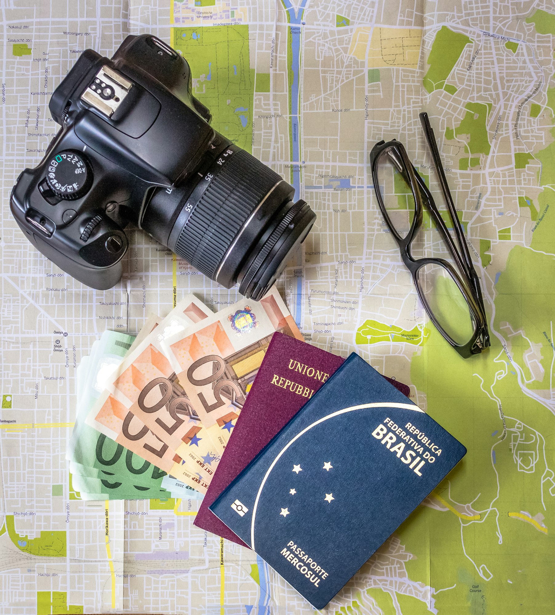 Brazilian and Italian passports on city map with euro bills money, camera and glasses